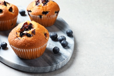 Photo of Stone board with blueberry muffins on light table, closeup view. Space for text