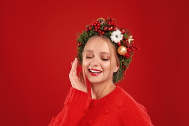 Beautiful young woman wearing Christmas wreath on red background