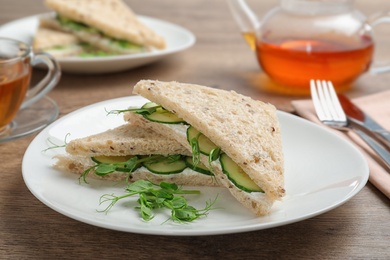 Photo of Plate with tasty cucumber sandwiches served on wooden table