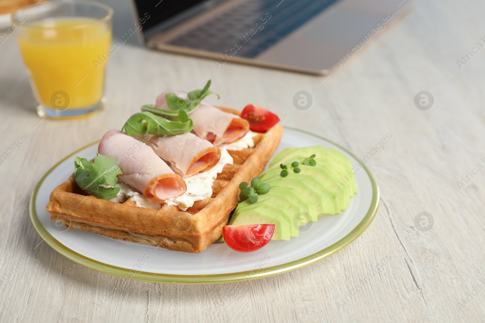 Photo of Delicious waffle with cheese, ham, tomatoes and avocado on wooden table