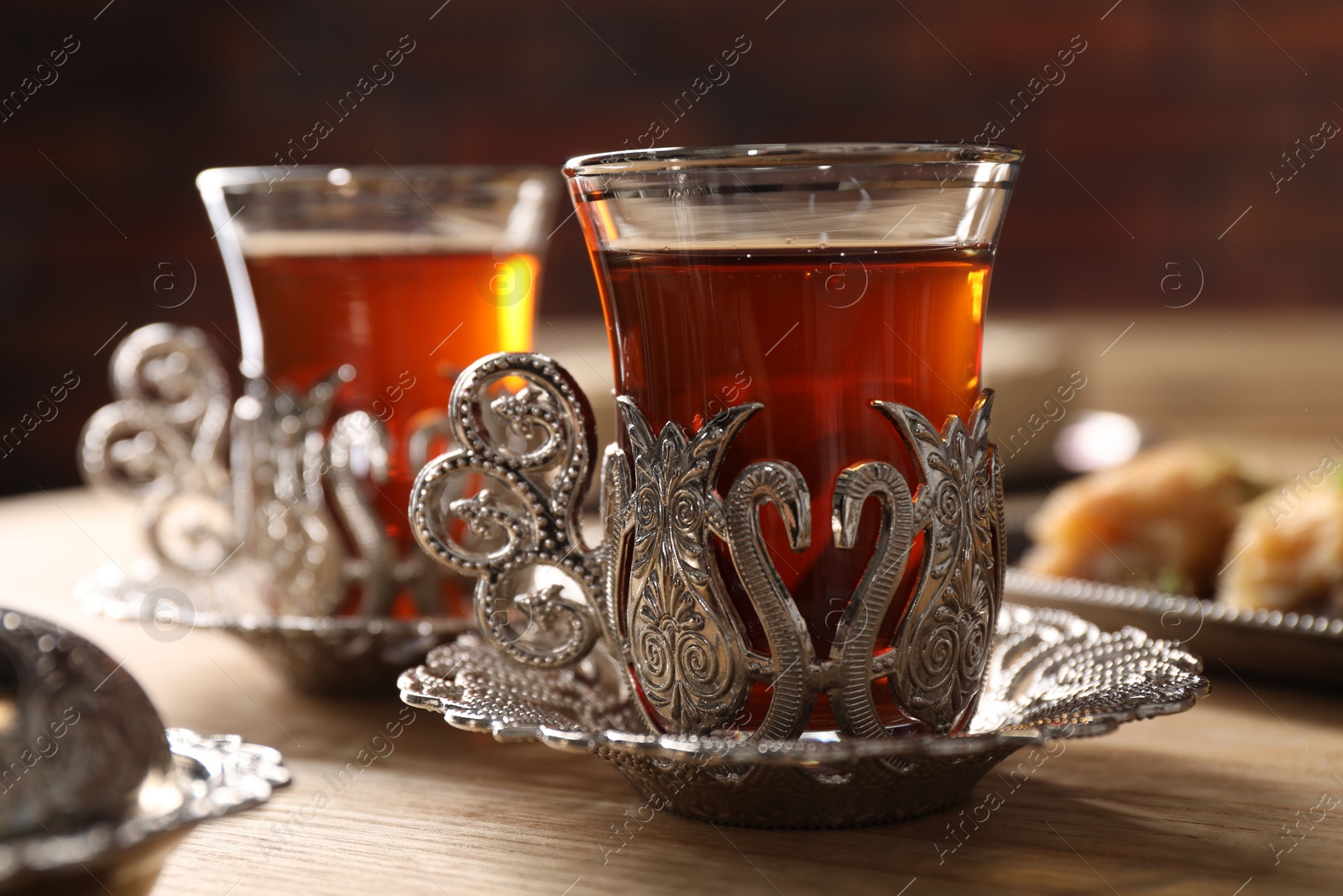 Photo of Glasses of traditional Turkish tea in vintage holders on wooden table, closeup