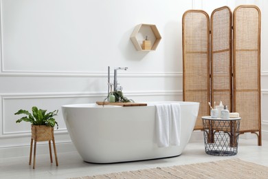 Photo of Modern ceramic bathtub and green plants near white wall in room