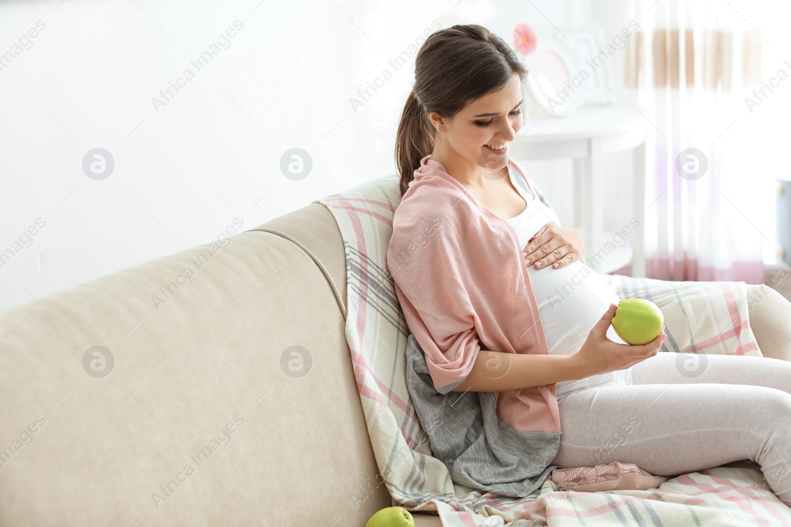 Photo of Young pregnant woman holding apple at home