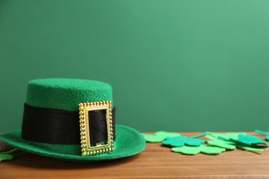 Leprechaun hat and decorative clover leaves on wooden table against green background, space for text. St Patrick's Day celebration