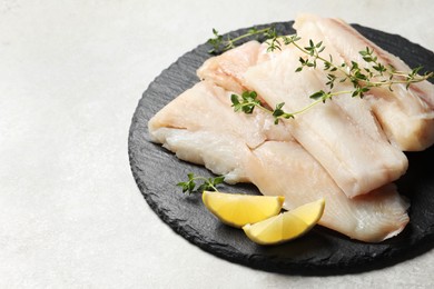 Photo of Pieces of raw cod fish and lemon on light grey table, space for text