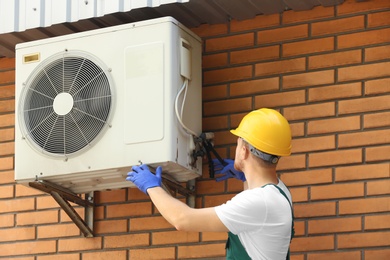 Photo of Professional technician repairing modern air conditioner outdoors