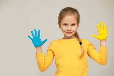 Photo of Little girl with hands painted in Ukrainian flag colors on light grey background, space for text. Love Ukraine concept