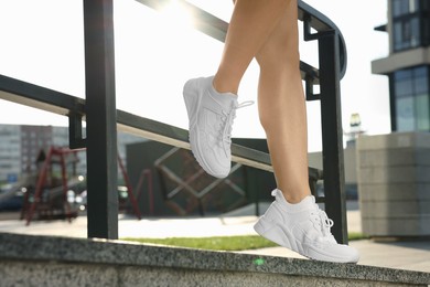 Woman wearing stylish sneakers near railing outdoors, closeup