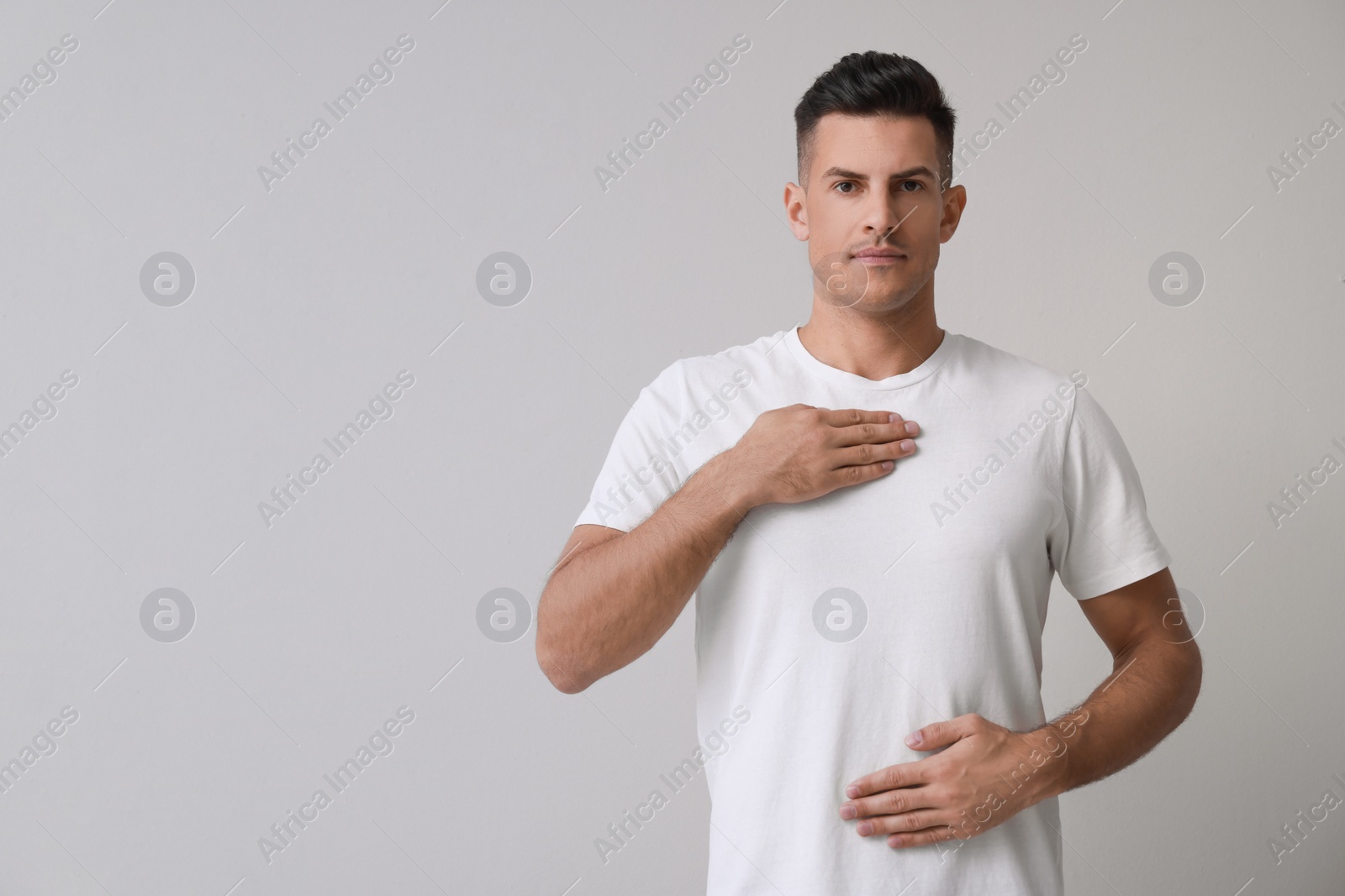 Photo of Handsome man holding hands near chest on grey background. Space for text