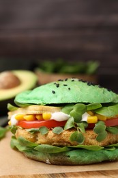 Tasty green vegan burger with vegetables, patty and microgreens on wooden table, closeup