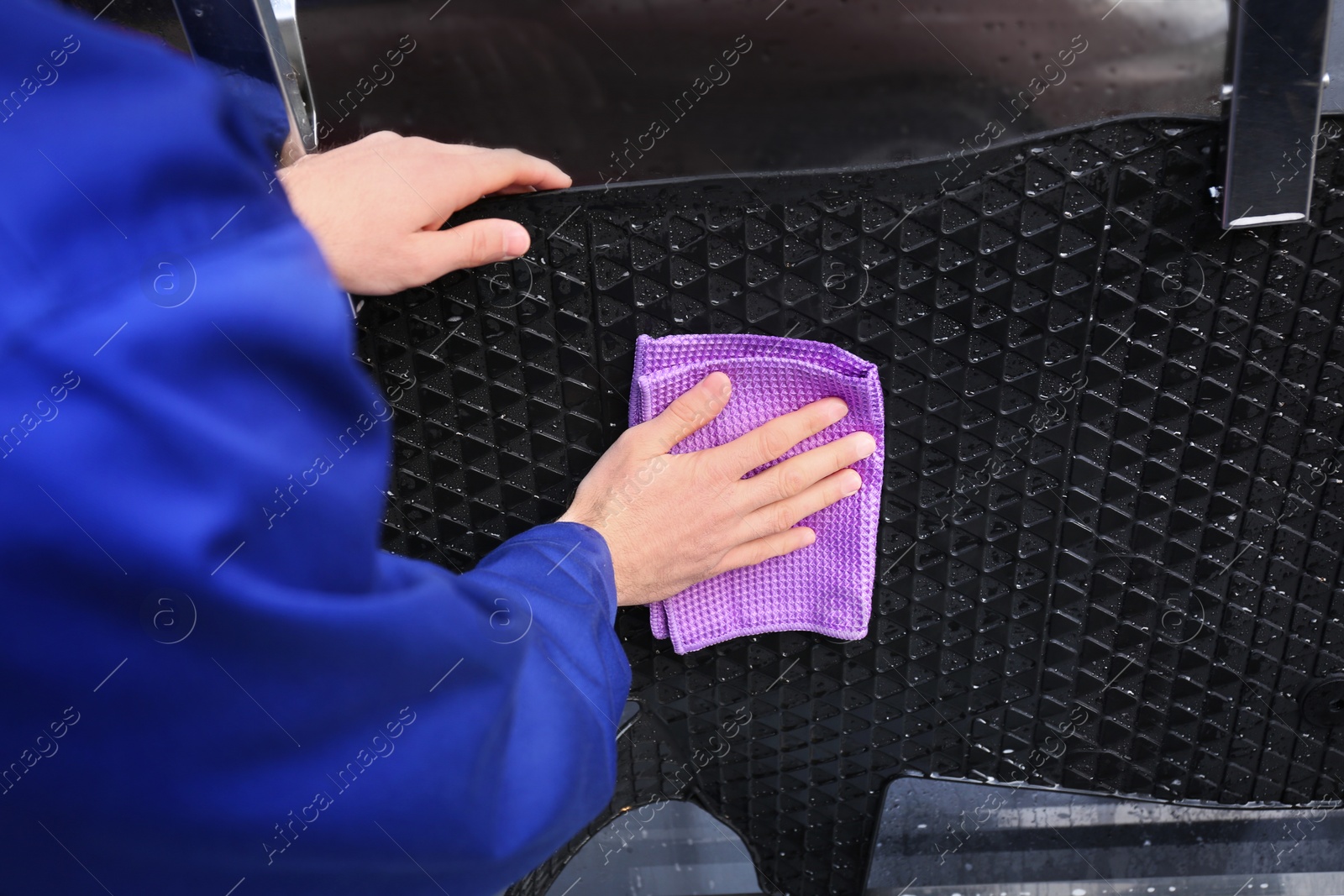 Photo of Worker wiping automobile floor mat at car wash, closeup