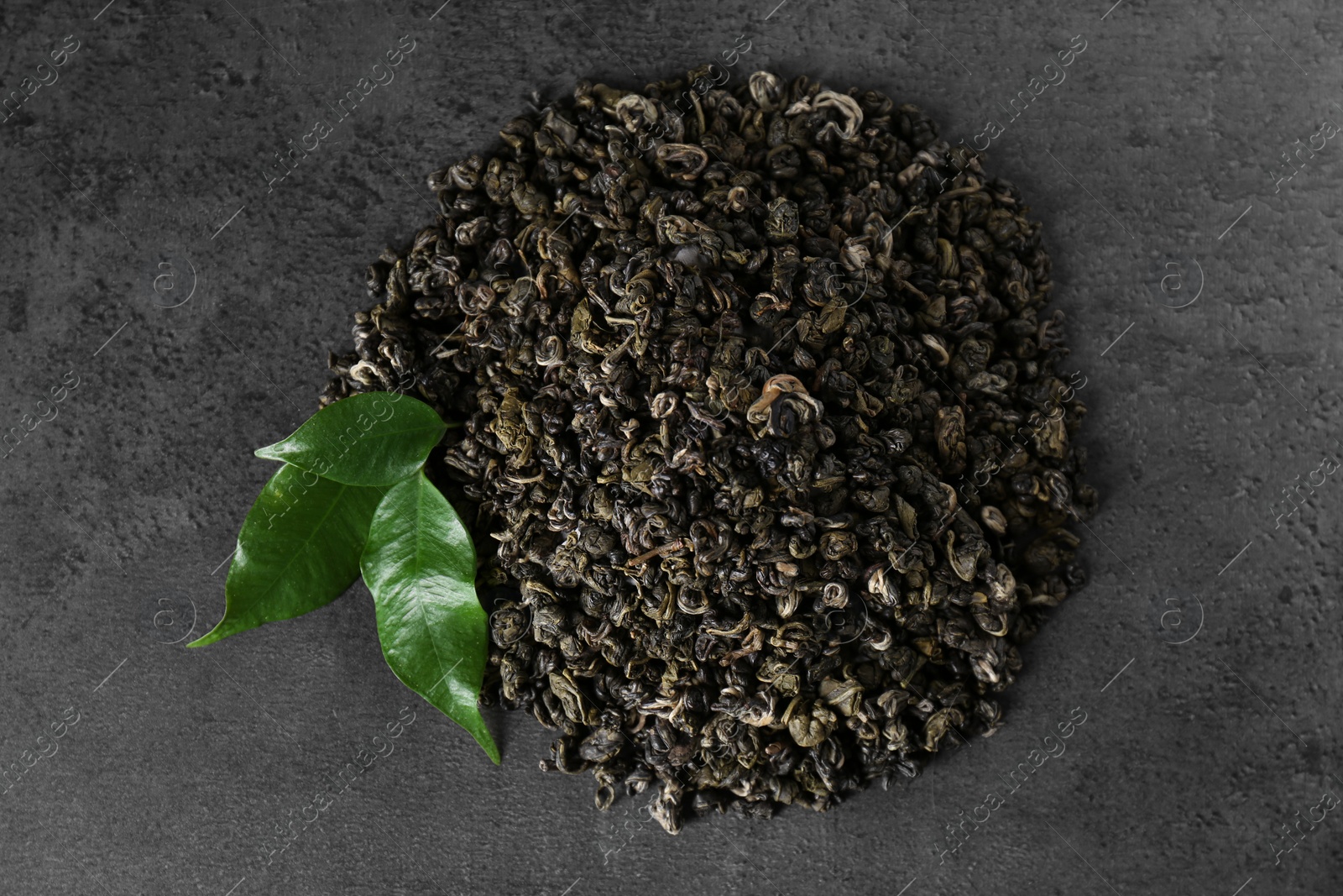 Photo of Heap of dried green tea leaves on grey table, top view