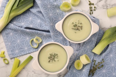 Tasty leek soup in bowls on white marble table, flat lay