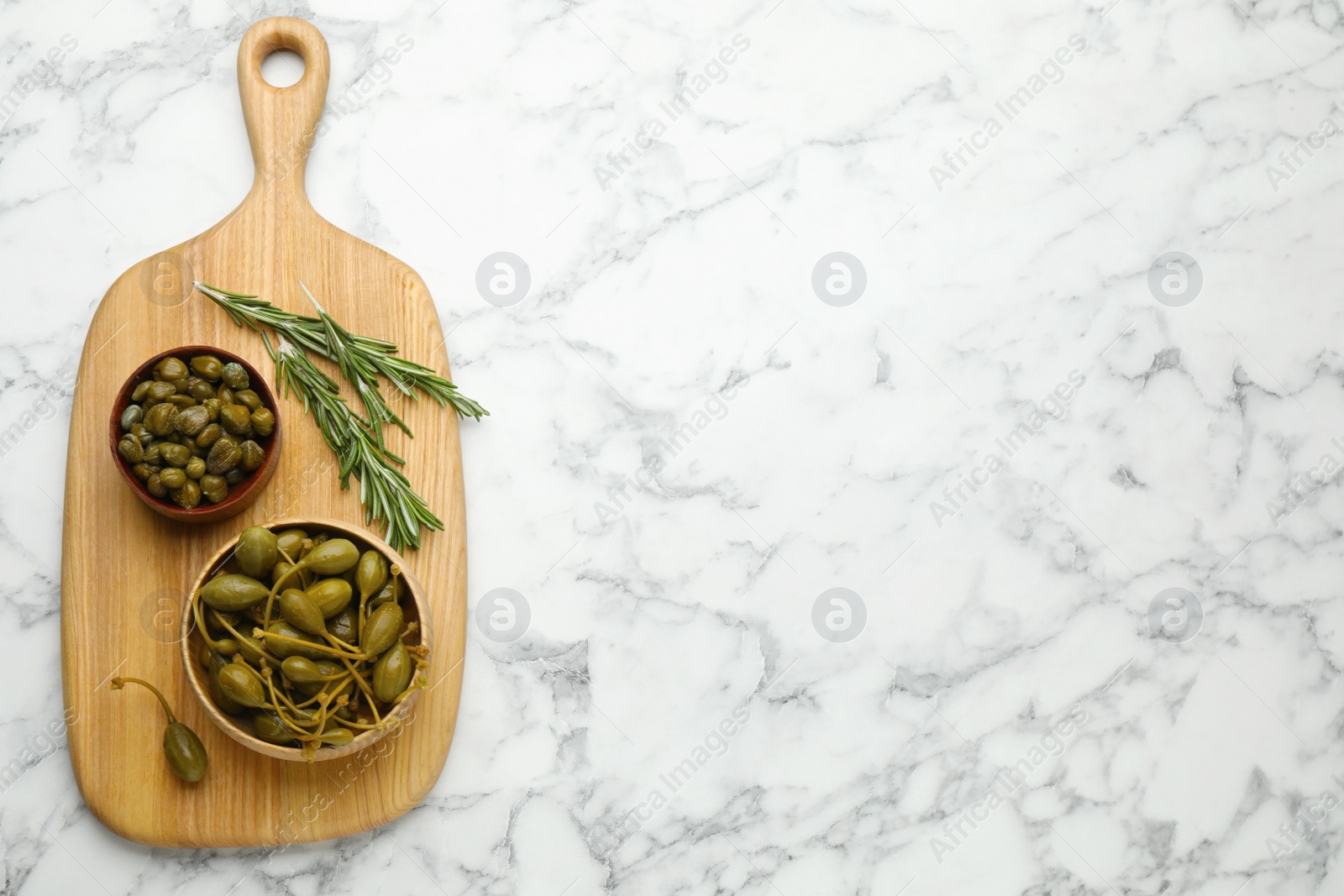 Photo of Delicious pickled capers and rosemary twigs on white marble table, top view. Space for text