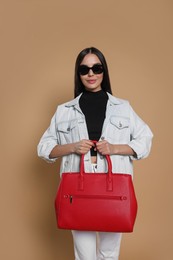 Young woman with stylish bag on beige background