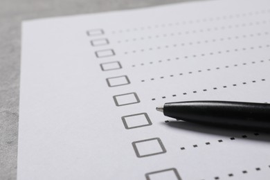 Paper sheet with checkboxes and pen on light grey table, closeup. Checklist