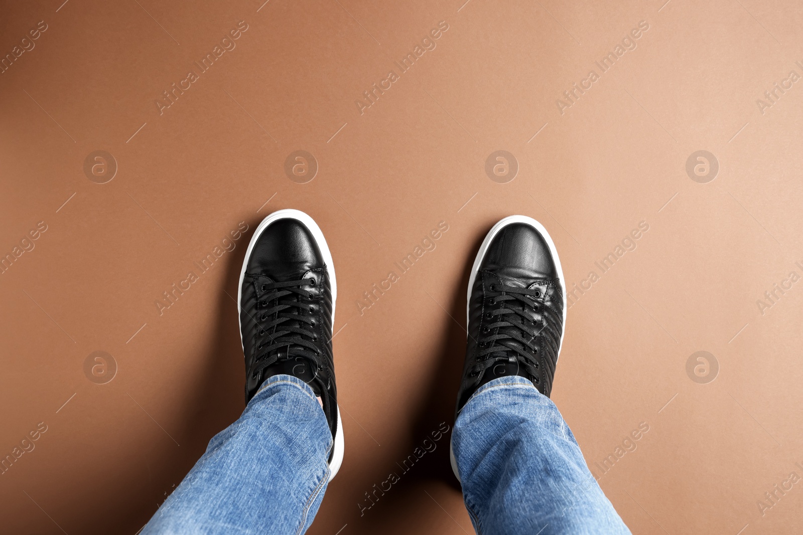 Photo of Man in black leather shoes standing on light brown background, top view