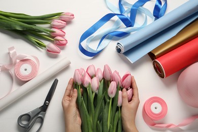 Woman making bouquet of beautiful fresh tulips at white wooden table, top view