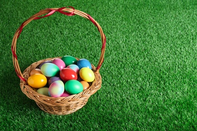 Photo of Wicker basket with Easter eggs on green grass. Space for text