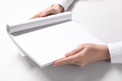Photo of Woman holding notebook with blank pages at white table, closeup. Mockup for design
