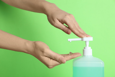 Photo of Woman applying antiseptic gel on hand against green background, closeup