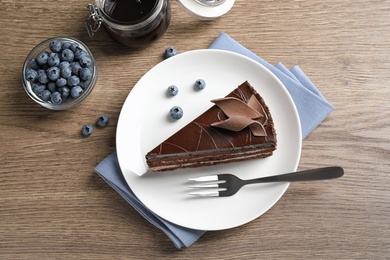 Photo of Delicious fresh chocolate cake served with blueberries on wooden table, flat lay