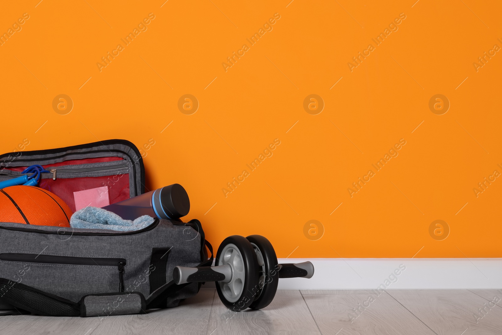 Photo of Gym bag and sports equipment on floor near orange wall, space for text