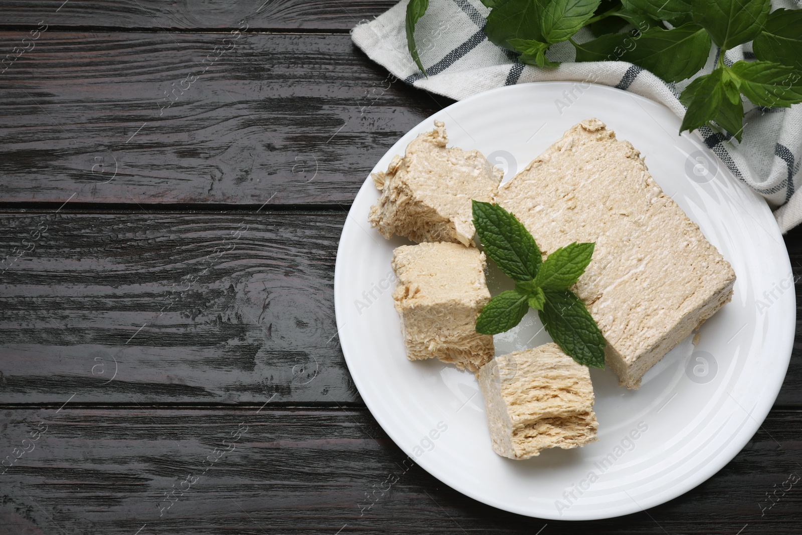 Photo of Plate with pieces of tasty halva and mint on wooden table, flat lay. Space for text