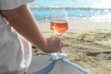 Photo of Woman with glass of tasty rose wine near sea, closeup