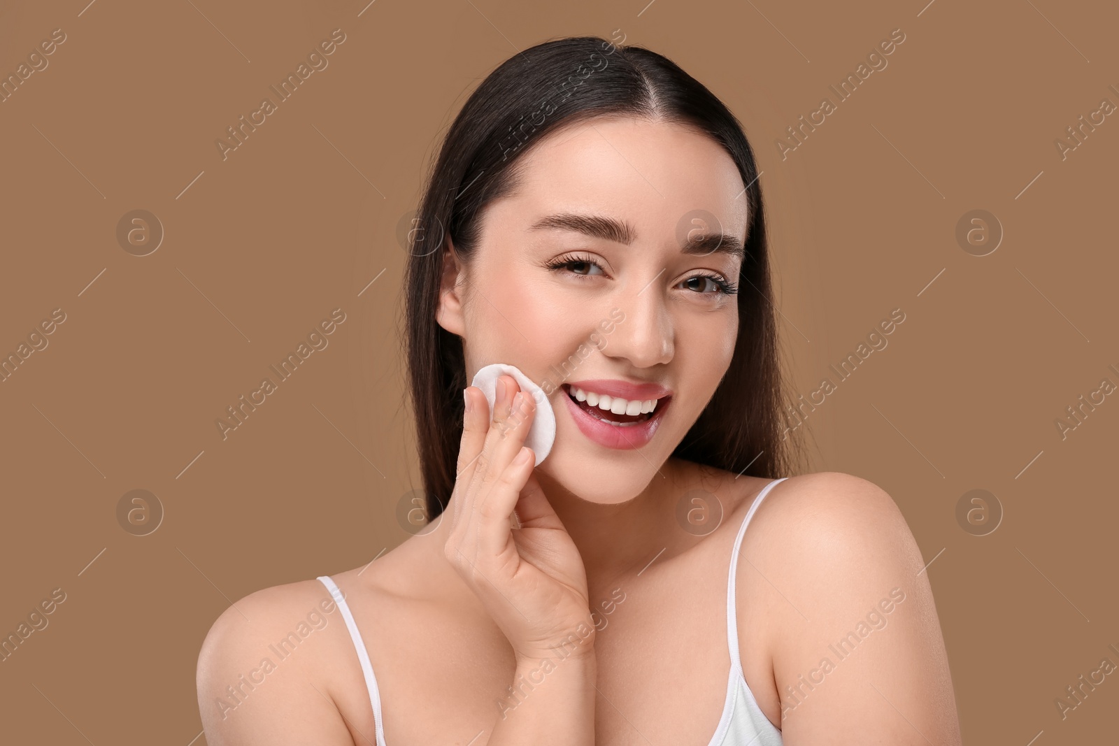 Photo of Beautiful woman removing makeup with cotton pad on beige background