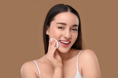 Photo of Beautiful woman removing makeup with cotton pad on beige background