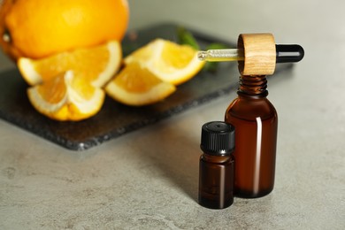 Bottles of citrus essential oil and pipette on grey table, space for text