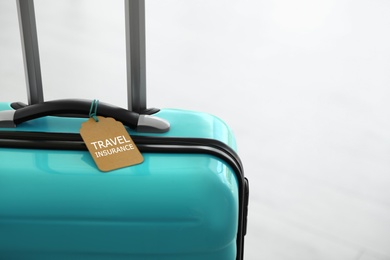Photo of Stylish suitcase with travel insurance label on light background, closeup. Space for text