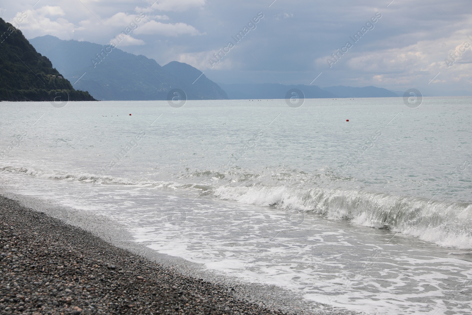 Photo of Picturesque view of beautiful sea shore and hills under sky with clouds