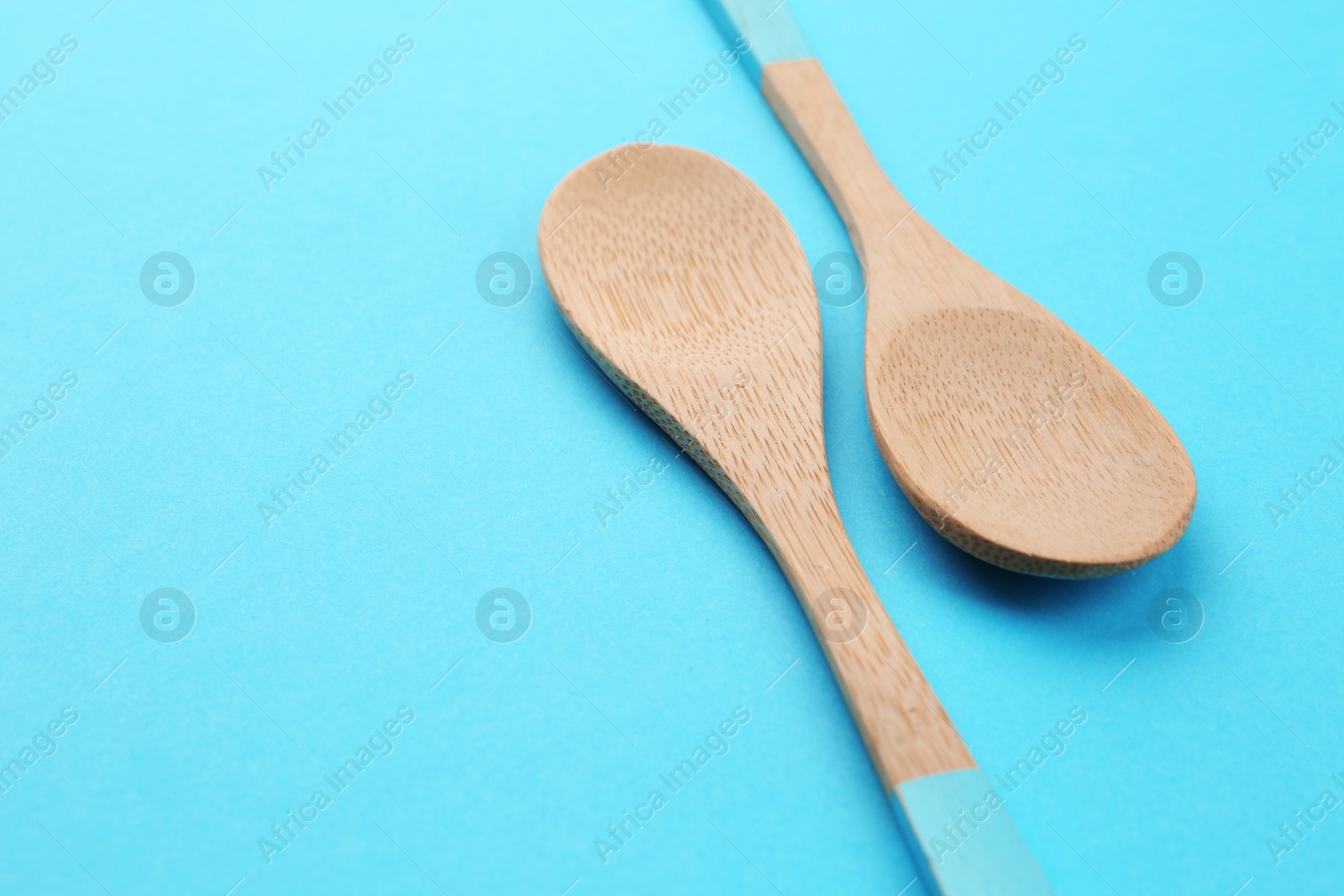 Photo of Clean empty bamboo spoons on blue background, space for text