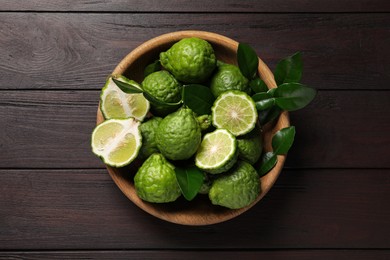 Photo of Whole and cut ripe bergamot fruits with green leaves in bowl on wooden table, top view