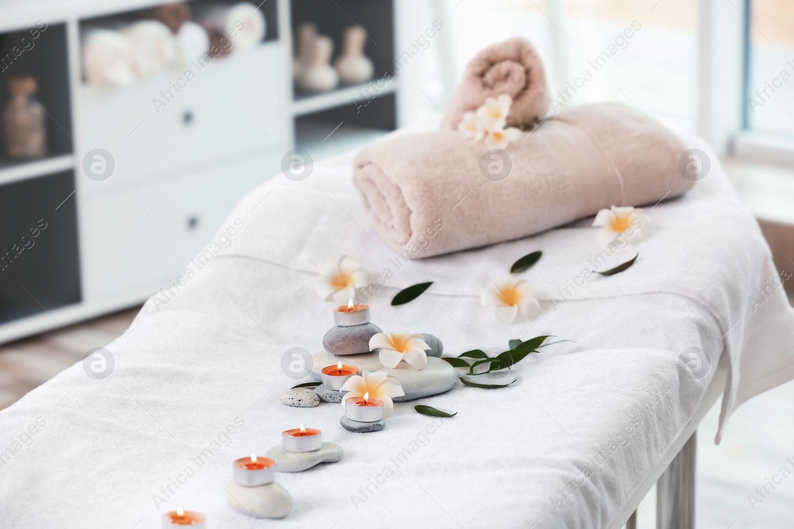 Photo of Towels, candles and stones on massage table in spa salon