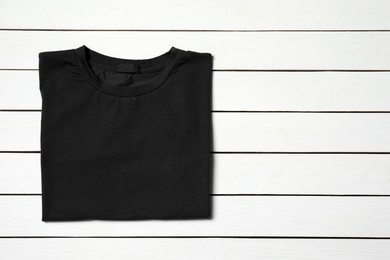 Photo of Stylish black T-shirt on white wooden table, top view. Space for text