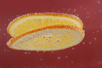 Photo of Fresh orange slices in sparkling water on red background