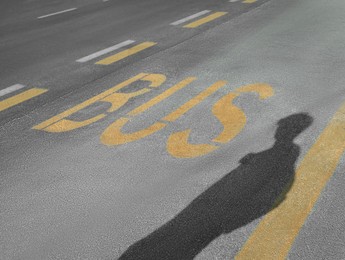 Bus stop pad and man's shadow on asphalt road