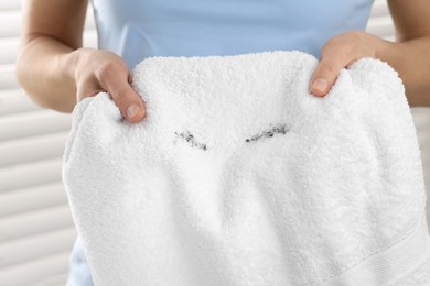 Woman holding terry towel with mascara spot indoors, closeup. Makeup removal