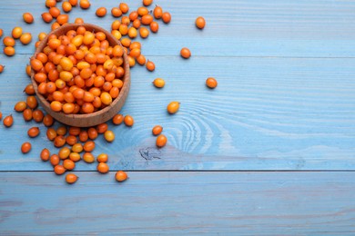 Photo of Bowl with fresh ripe sea buckthorn berries on light blue wooden table, above view. Space for text