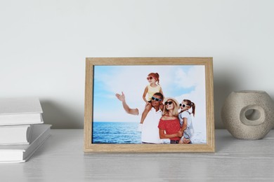 Photo of Frame with family photo, books and other decor element on white wooden table indoors