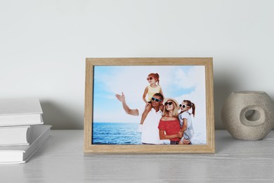 Frame with family photo, books and other decor element on white wooden table indoors