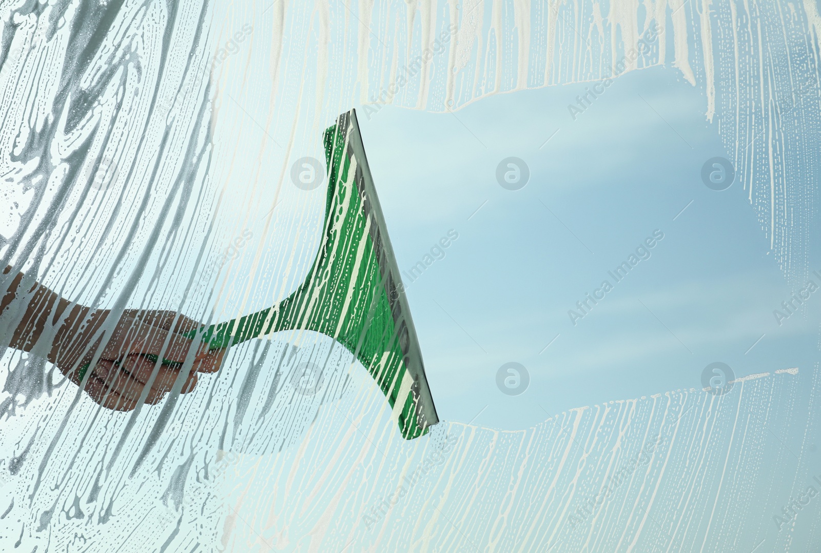 Photo of Woman cleaning window with squeegee on spring day, closeup