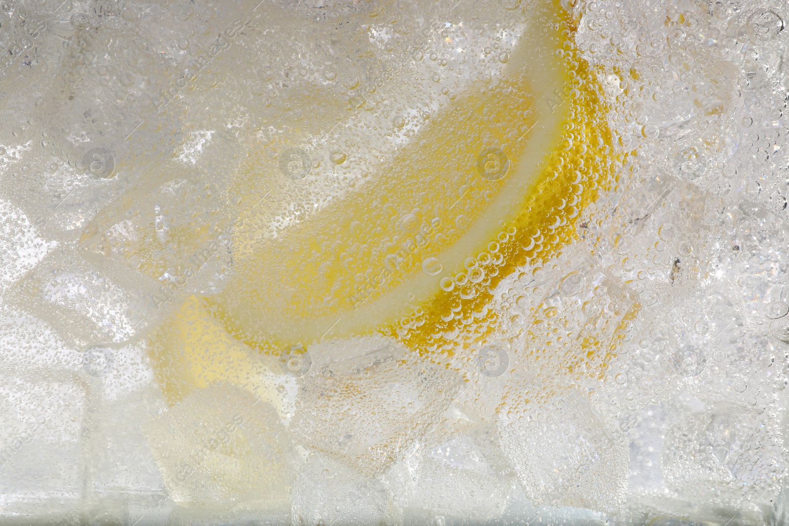 Photo of Juicy lemon slice and ice cubes in soda water on white background, closeup