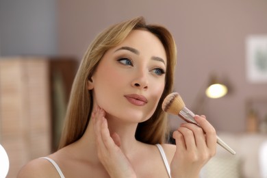 Photo of Reflection of beautiful young woman applying face powder with brush in mirror at home