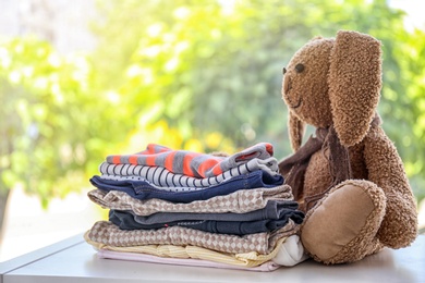 Stack of stylish child clothes and toy bunny on table against blurred background