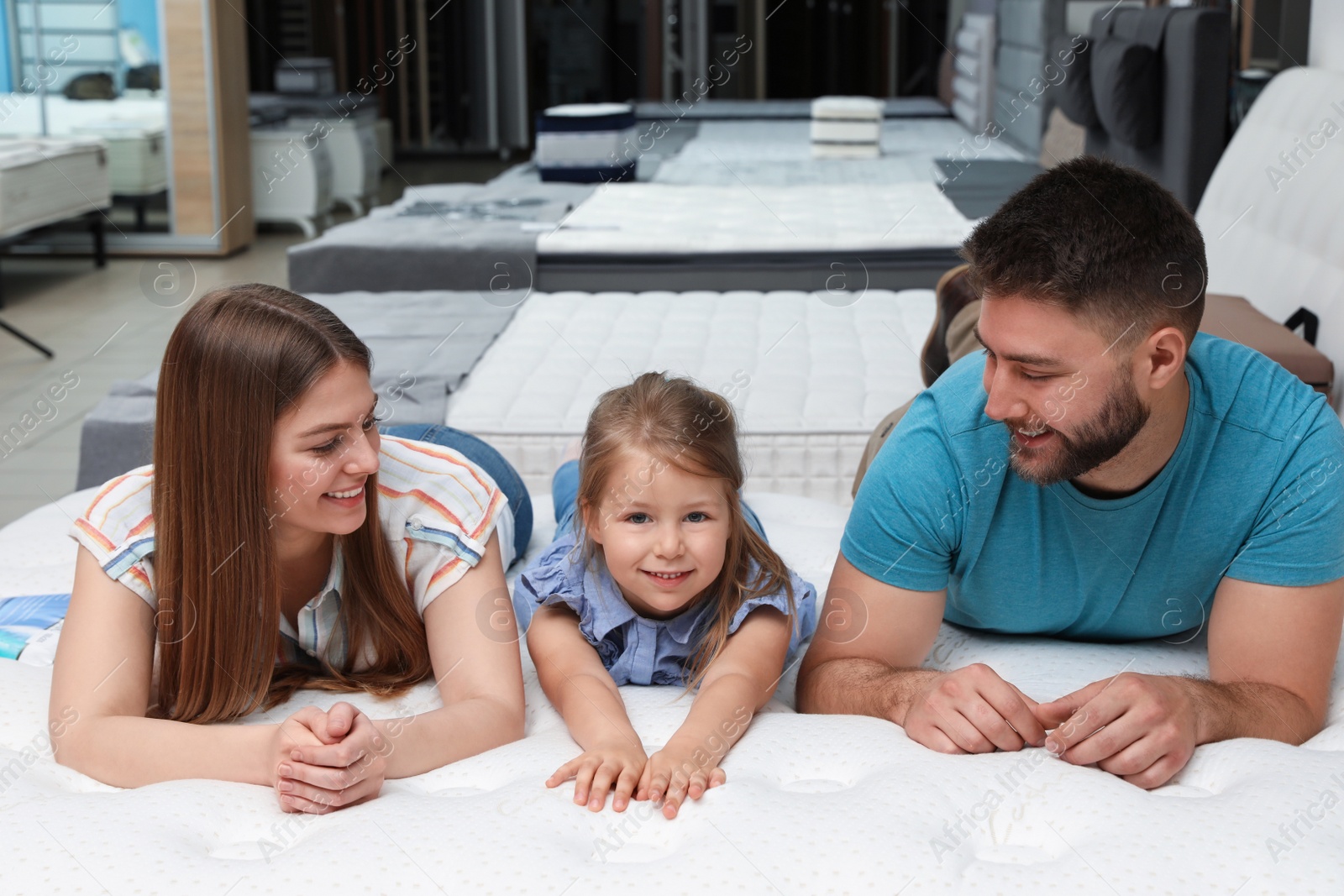 Photo of Happy family lying on new orthopedic mattress in store