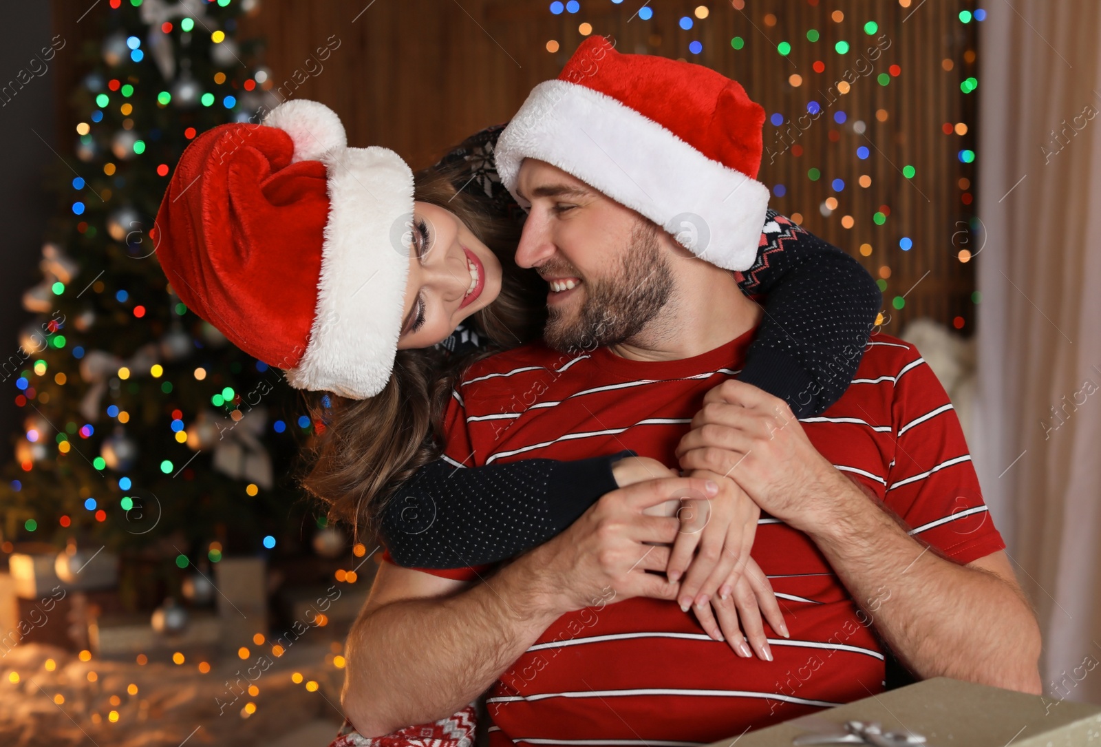 Photo of Happy young couple in Santa hats celebrating Christmas at home